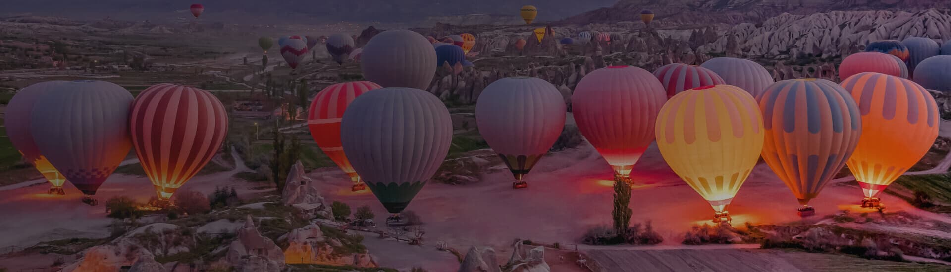 Hot air balloons glowing over a rocky mountain valley at dusk